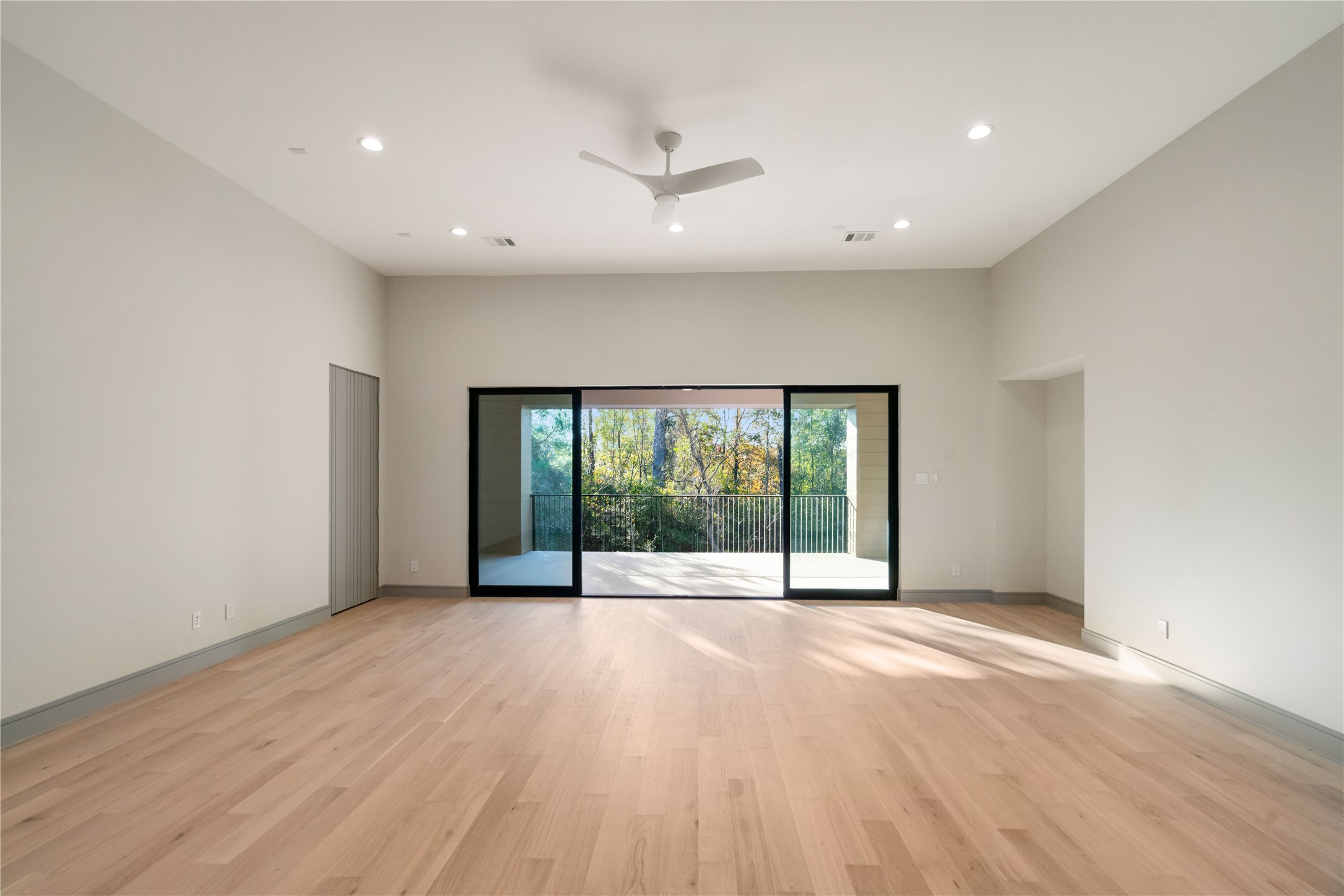 47 Pronghorn Place Spring, TX 77389 - Photo 36 of 44 This spacious living area features light wood flooring, neutral walls, and a ceiling fan. Large sliding glass doors open to a balcony with a view of trees, providing ample natural light.