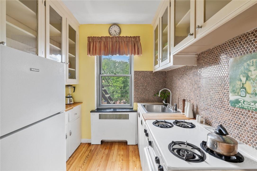 4445 Post Road, Unit 7D Bronx, NY 10471 - Photo 7 of 13 Kitchen with white fridge, tasteful backsplash, sink, radiator, and light hardwood / wood-style floors