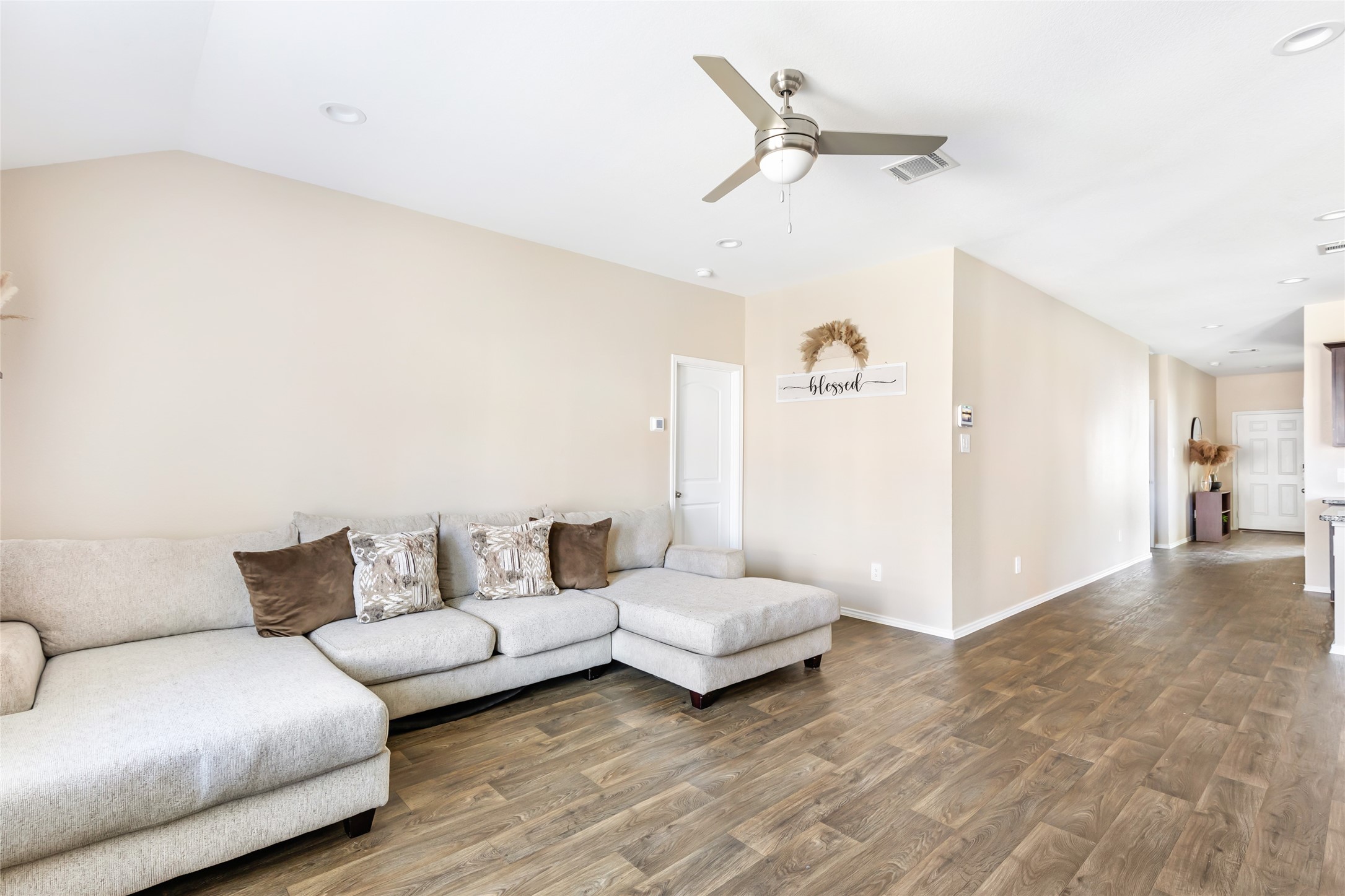 811 Republic Road New Caney, TX 77357 - Photo 30 of 37 This spacious living area features wood-style flooring, a neutral color palette, and a large sectional sofa. The room is well-lit with recessed lighting and a ceiling fan, and it flows into an open hallway leading to other areas of the home.
