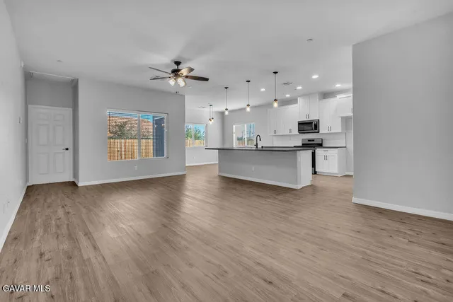 an empty room with wooden floor kitchen view and a ceiling fan