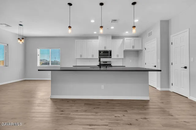 a large kitchen with stainless steel appliances granite countertop a stove a sink a refrigerator and white cabinets with wooden floor