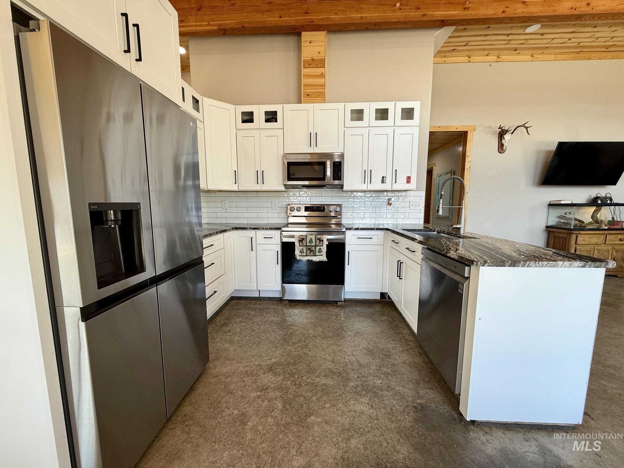 929 Mt Idaho Grade Road Grangeville, ID 83530 - Photo 10 of 47 Kitchen with stainless steel appliances, a peninsula, backsplash, white cabinetry, and glass insert cabinets
