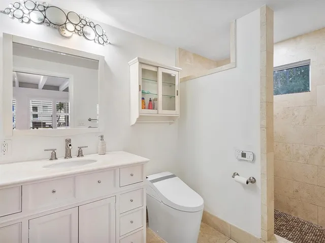 a bathroom with a toilet a sink a mirror a shower a vanity and window