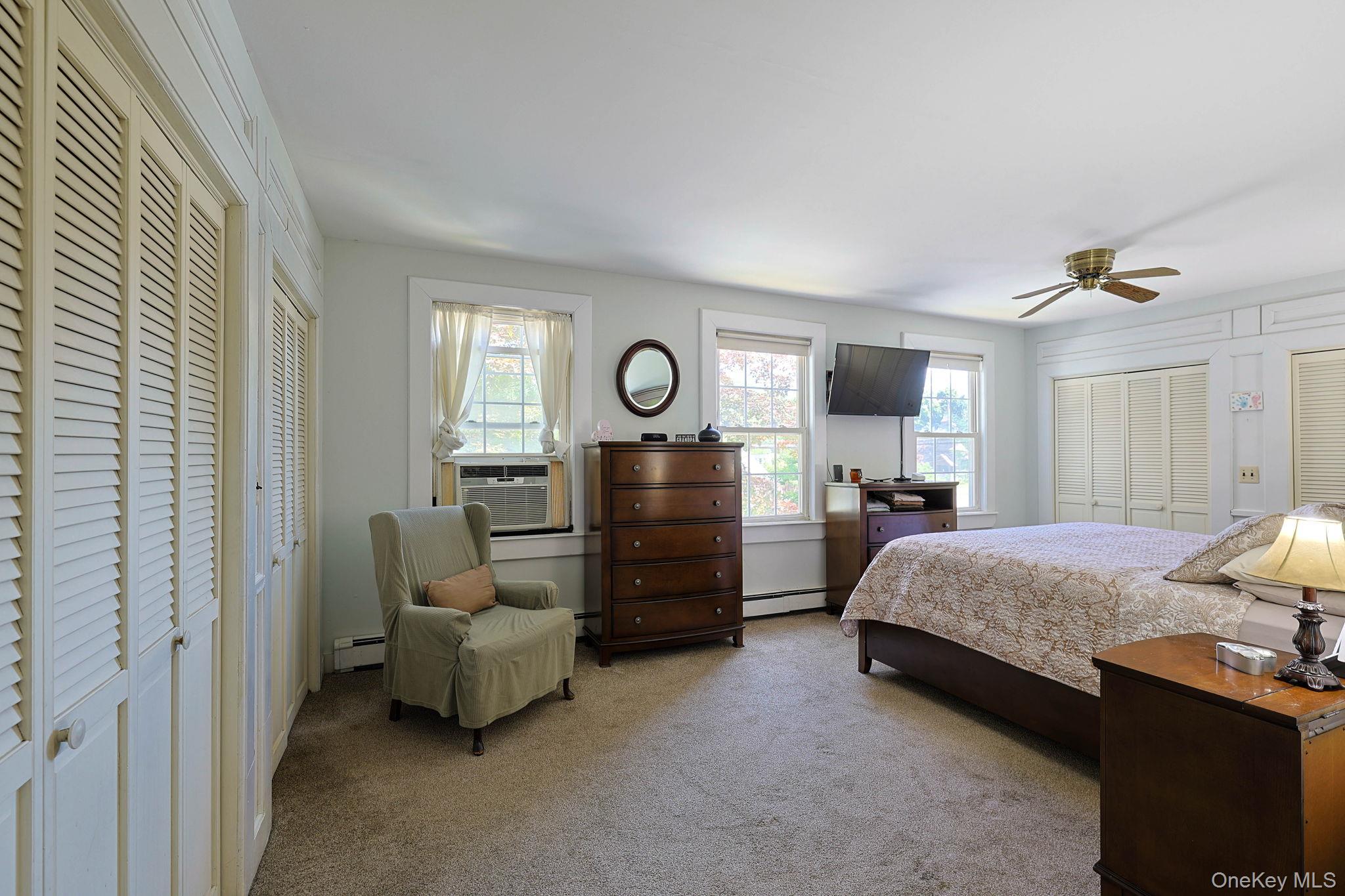 9 Library Road Tuxedo Park, NY 10987 - Photo 16 of 37 Carpeted room Primary bedroom featuring multiple windows with natural light, two sets of louvered bi-fold doors, and a ceiling fan