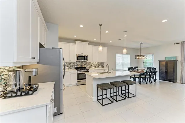 a kitchen with stainless steel appliances kitchen island granite countertop a stove a refrigerator a sink a dining table and chairs