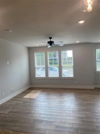 an empty room with wooden floor fan and windows