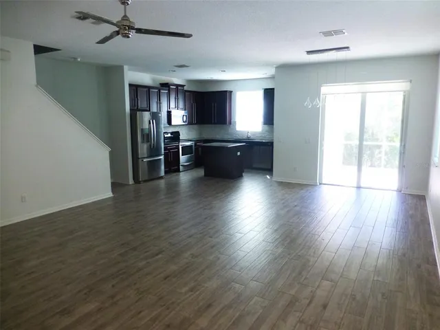 an empty room with wooden floor a ceiling fan and windows