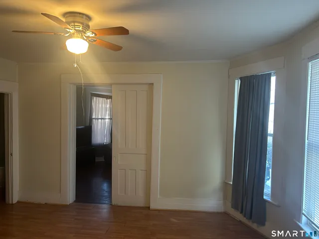 a view of an empty room with wooden floor and fan