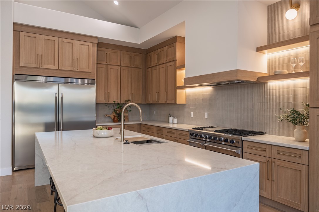 8800 Lusso Las Vegas, NV 89134 - Photo 31 of 85 Kitchen with light stone counters, high quality appliances, backsplash, a center island with sink, and light wood finished floors