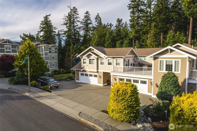 a view of a white house next to a yard with potted plants and large trees