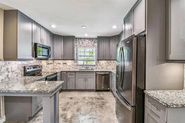 a kitchen with granite countertop stainless steel appliances a sink stove refrigerator and cabinets
