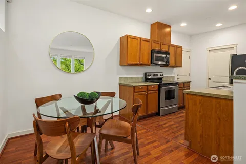 a kitchen with stainless steel appliances granite countertop a stove top oven a sink a dining table and chairs with wooden floor