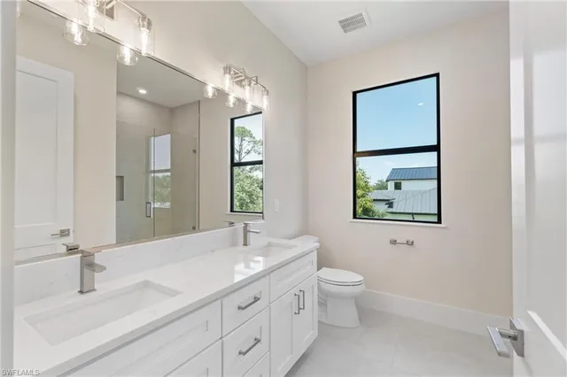 a bathroom with a double vanity sink toilet a large mirror a shower and a window
