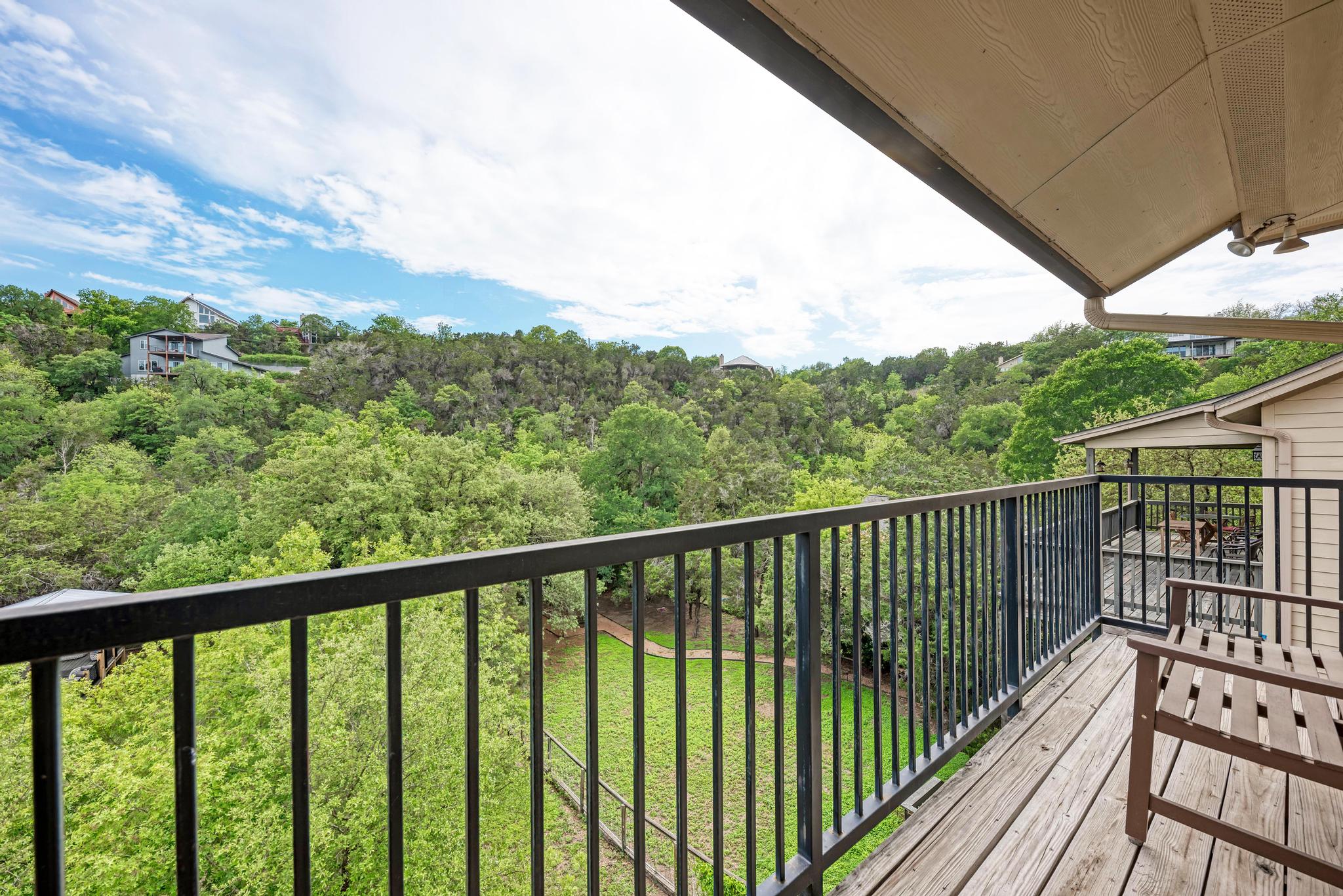2605 Indian Creek Road Austin, TX 78734 - Photo 13 of 33 Outdoor wood-finish deck with black metal railings, offering an elevated perspective of the surrounding tree-lined hills and a partial view of a lower-level deck