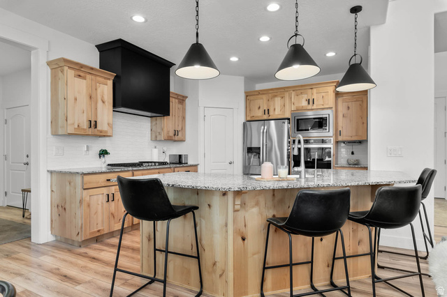 500 North 516th Street West, Unit 19 Mapleton, UT 84664 - Photo 7 of 41 Modern kitchen featuring natural wood cabinetry, a large kitchen island with seating, stainless steel appliances, a white subway tile backsplash, and wood-finish flooring