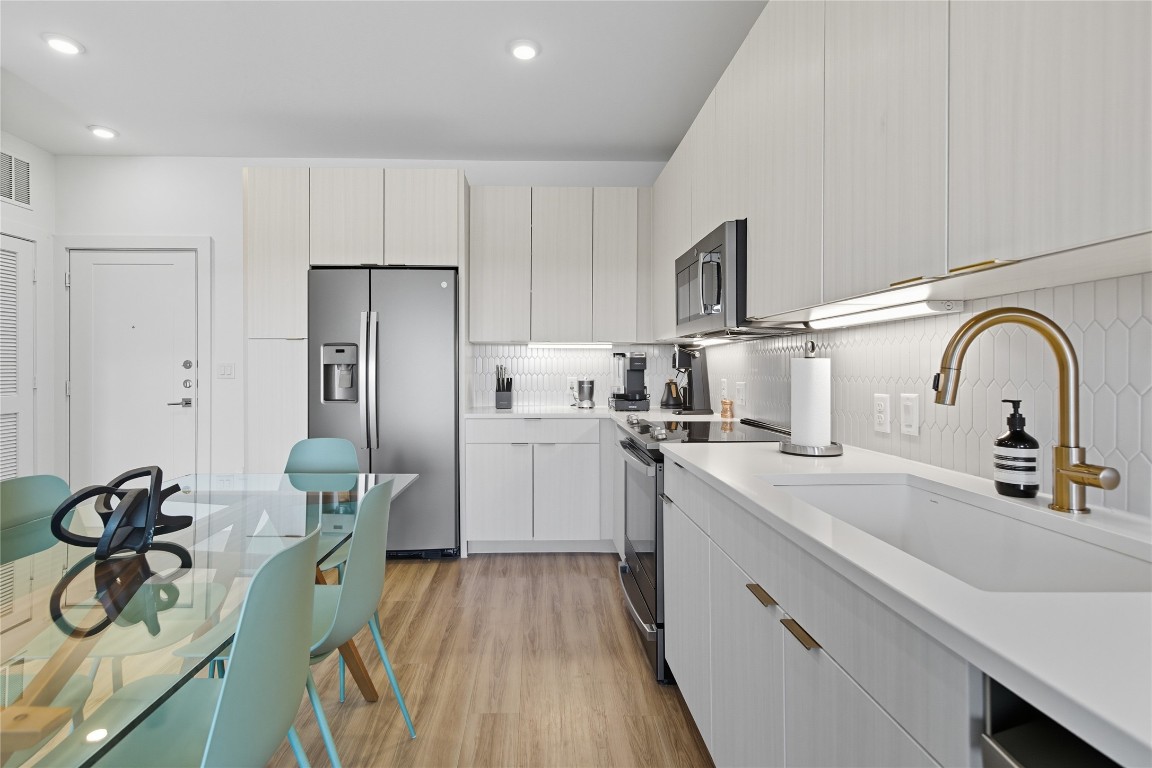 4802 South Congress Avenue, Unit 507 Austin, TX 78745 - Photo 9 of 30 Kitchen with modern cabinets, appliances with stainless steel finishes, light wood-style flooring, backsplash, and light stone countertops