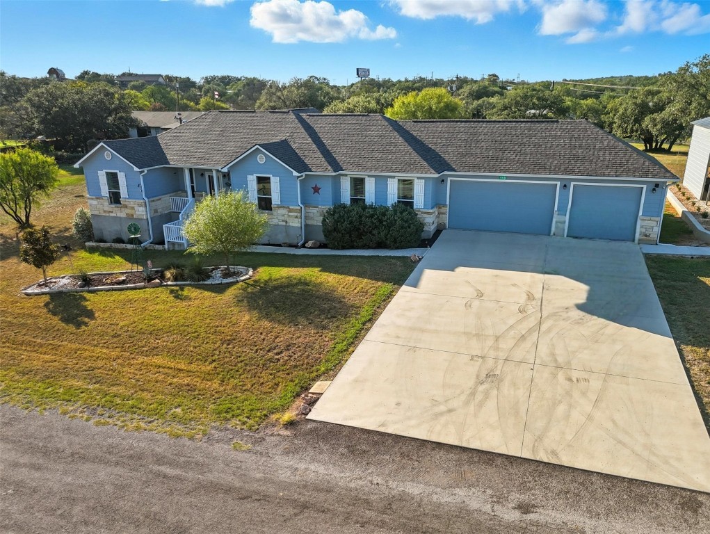 Single story home with stone siding, driveway, a shingled roof, a front lawn, and an attached garage