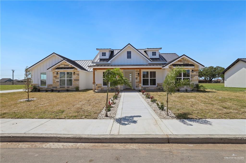 View of front of property with board and batten siding, stone siding, a front yard, a standing seam roof, and metal roof