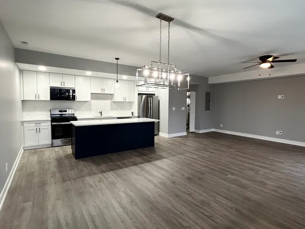 a room with stainless steel appliances kitchen island granite countertop a sink dishwasher a refrigerator and a fireplace with wooden floor