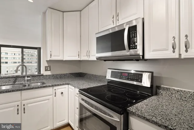 a kitchen with stainless steel appliances granite countertop white cabinets and a stove top oven