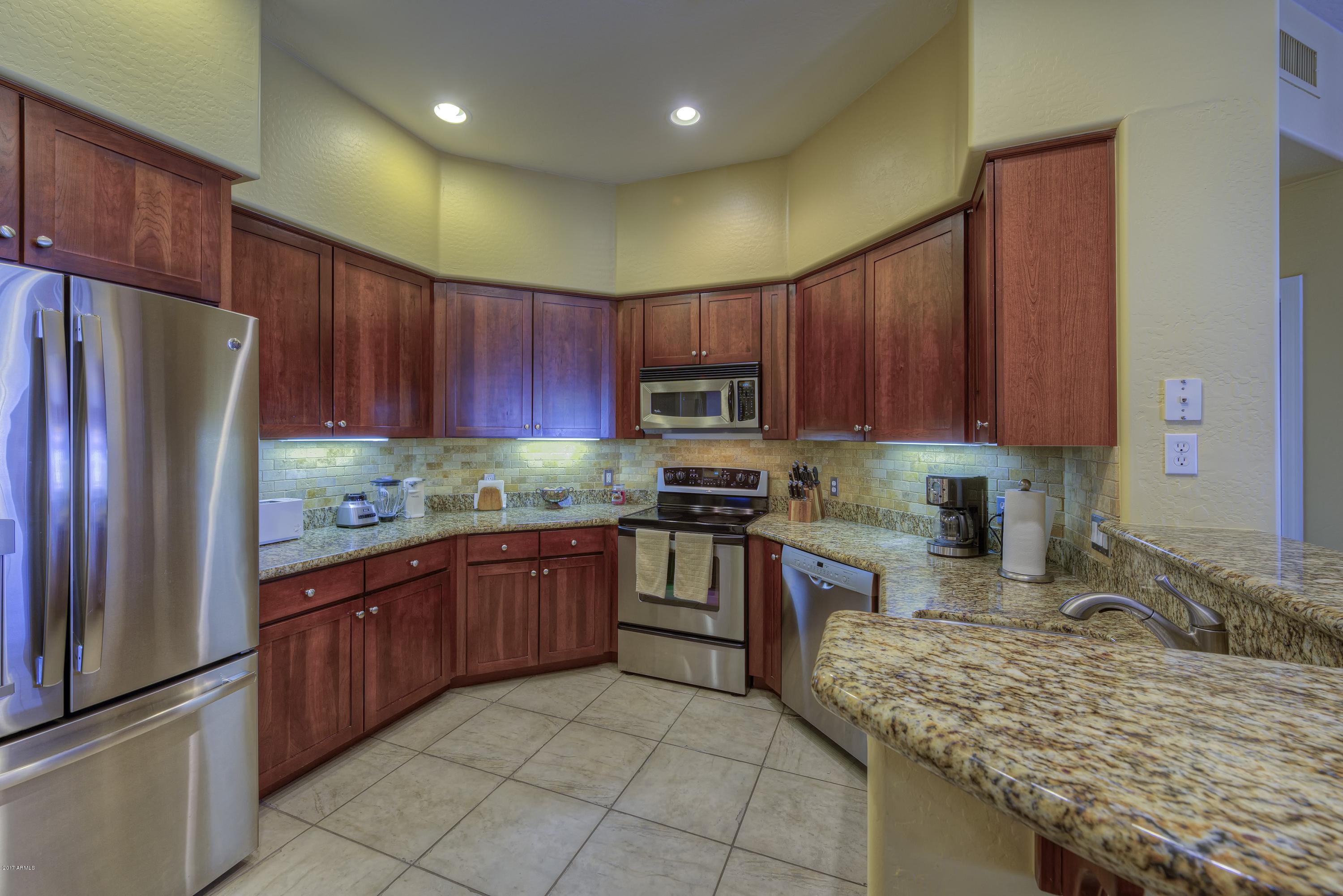 4488 East Thomas Road, Unit 2046 Phoenix, AZ 85018 - Photo 6 of 18 a kitchen with granite countertop wooden cabinets a refrigerator and a sink