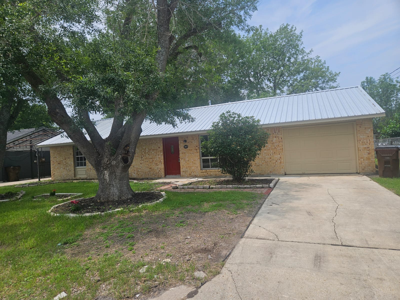 1401 Trinity Street Lockhart, TX 78644 - Photo 3 of 31 Single-story residence featuring a metal roof, brick exterior, and an attached garage with a light-colored door