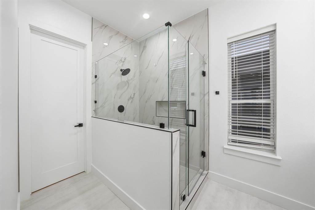 306 East 7th Street Dallas, TX 75203 - Photo 14 of 22 Walk-in shower with clear glass enclosure and black hardware, featuring large format wall tile with subtle veining and a recessed niche