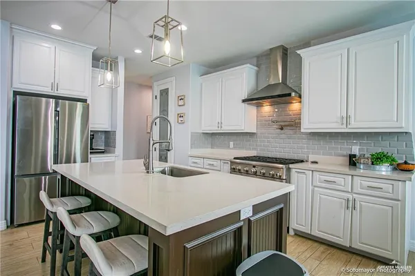 a kitchen with kitchen island granite countertop a stove a sink a refrigerator and white cabinets with wooden floor