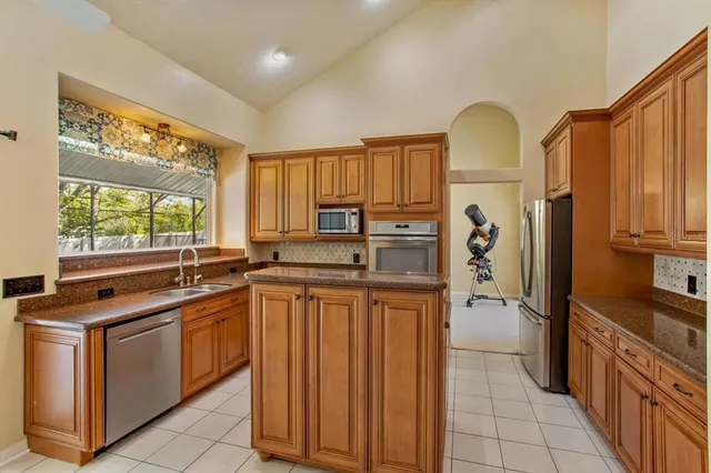 a kitchen with stainless steel appliances granite countertop a stove top oven a sink dishwasher and a refrigerator with wooden cabinets