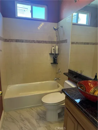 a bathroom with a granite countertop bathtub shower sink vanity and toilet