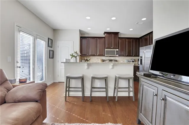 a living room with stainless steel appliances furniture a flat screen tv and kitchen view
