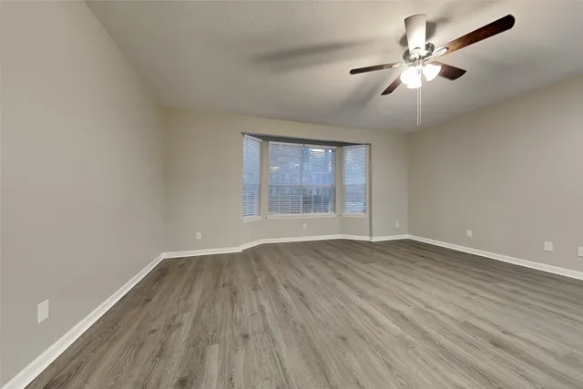 an empty room with wooden floor chandelier fan and windows