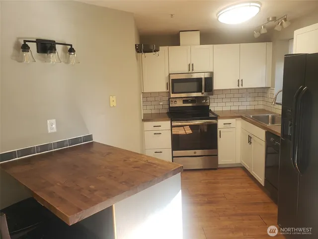 a kitchen with stainless steel appliances granite countertop a stove a refrigerator a sink and white cabinets