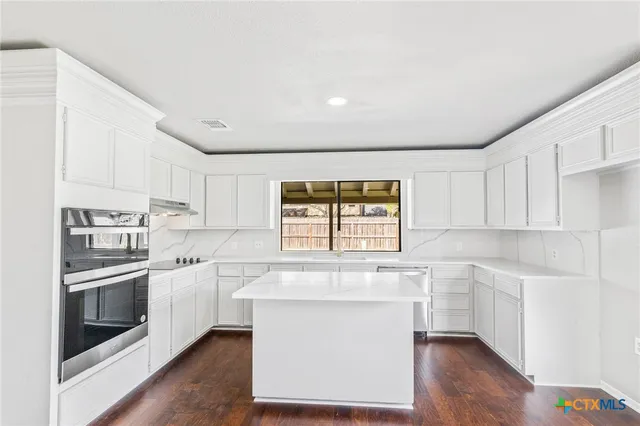 a kitchen with stainless steel appliances granite countertop a stove a sink and white cabinets with wooden floor