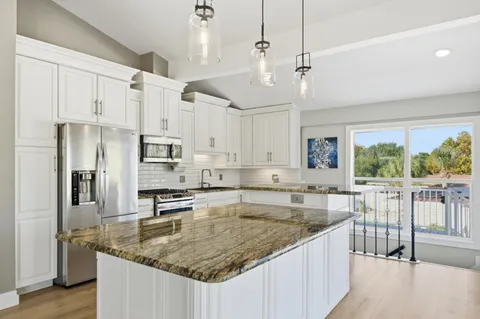 a kitchen with stainless steel appliances granite countertop a sink a refrigerator a center island a stove and white cabinets with wooden floor