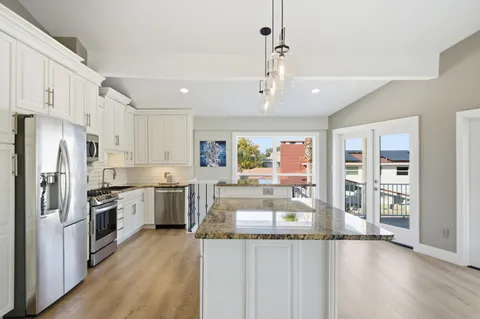 a kitchen with stainless steel appliances granite countertop a refrigerator a stove oven and white cabinets with wooden floors