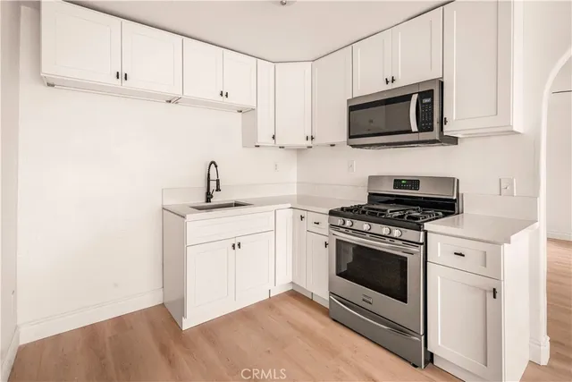 a kitchen with stainless steel appliances granite countertop white cabinets a sink a stove a microwave and view living room