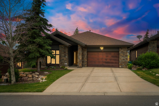4892 Eagle Rdg Drive Eden, UT 84310 - Photo 1 of 39 Stone and wood exterior featuring a peaked roofline, an attached garage with a wood-finish door, a concrete driveway, and established landscaping with mature trees and rock elements
