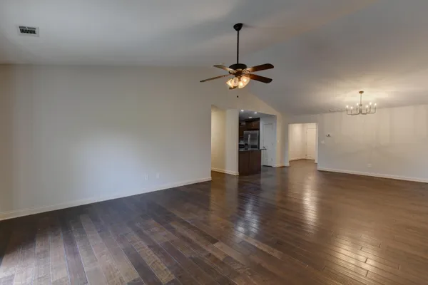 a view of an empty room with wooden floor and a ceiling fan
