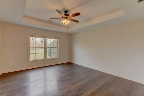 an empty room with wooden floor chandelier fan and windows