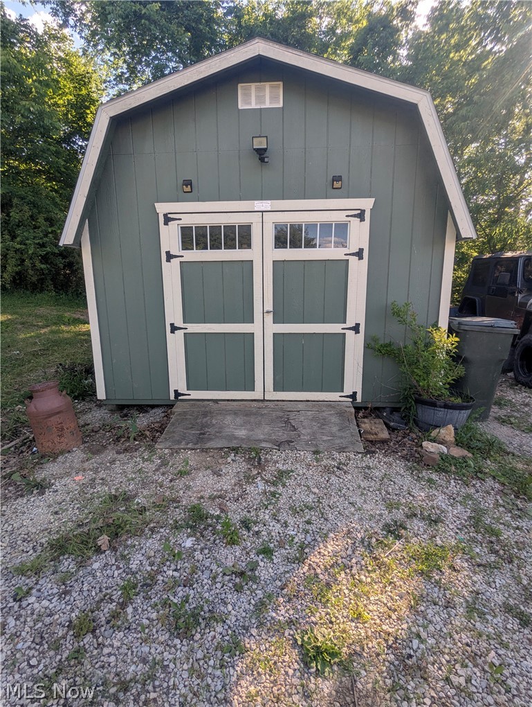 17960 Raven Road Salesville, OH 43778 - Photo 27 of 27 Gable-style shed featuring a green exterior with white trim, double doors with transom-style window inserts, and exterior lighting