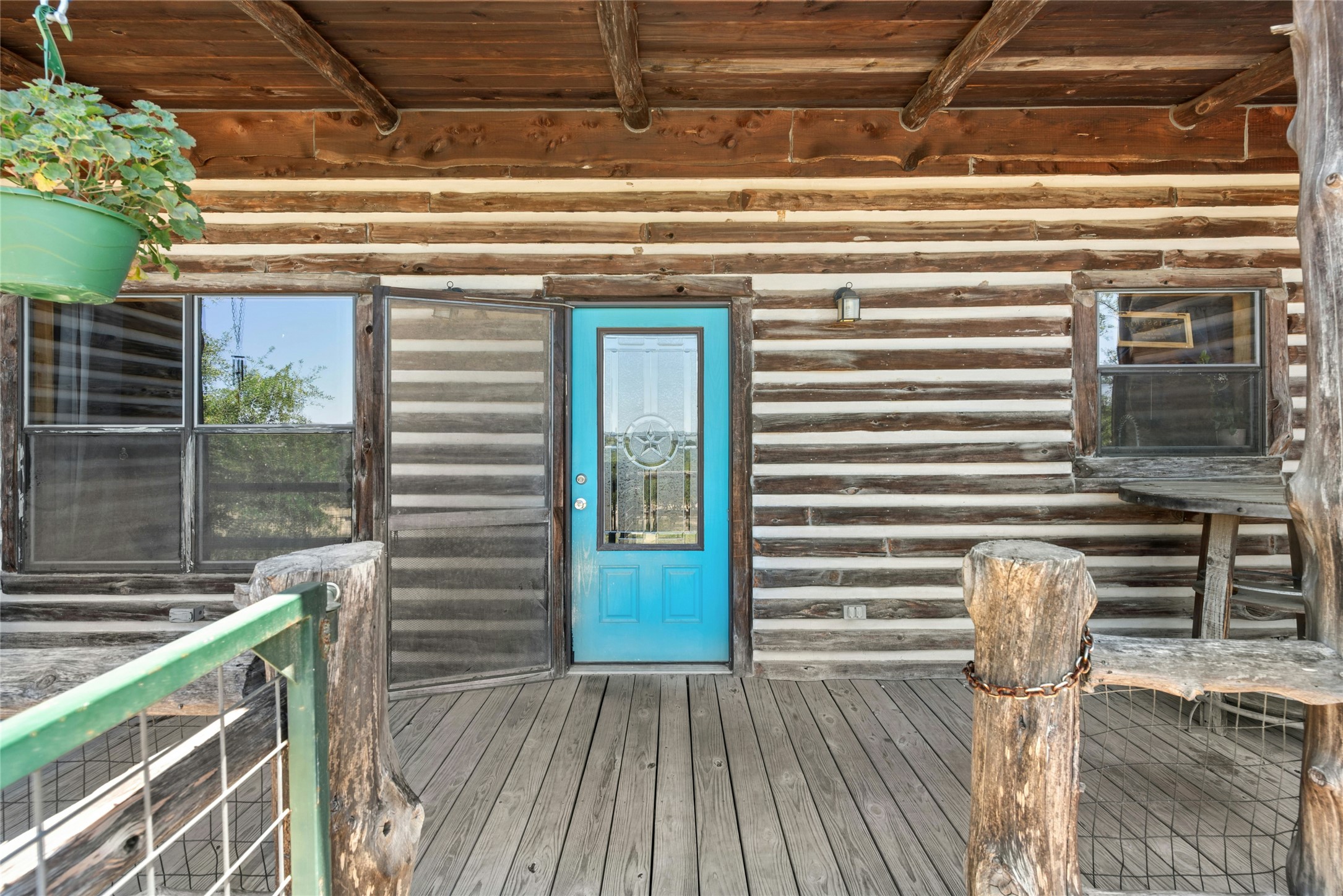 496 Middleton Road Spicewood, TX 78669 - Photo 26 of 40 Expansive wood-plank porch featuring a vibrant blue entry door with a glass insert, a log cabin exterior, and natural wood support beams