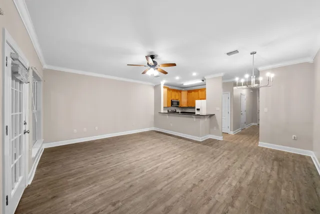 an empty room with wooden floor a chandelier fan and windows