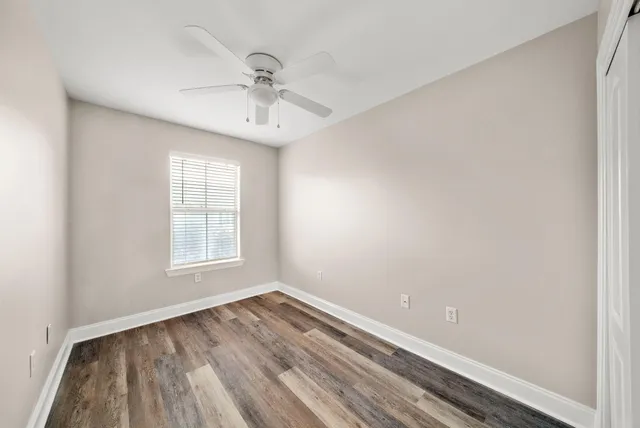 an empty room with wooden floor fan and windows