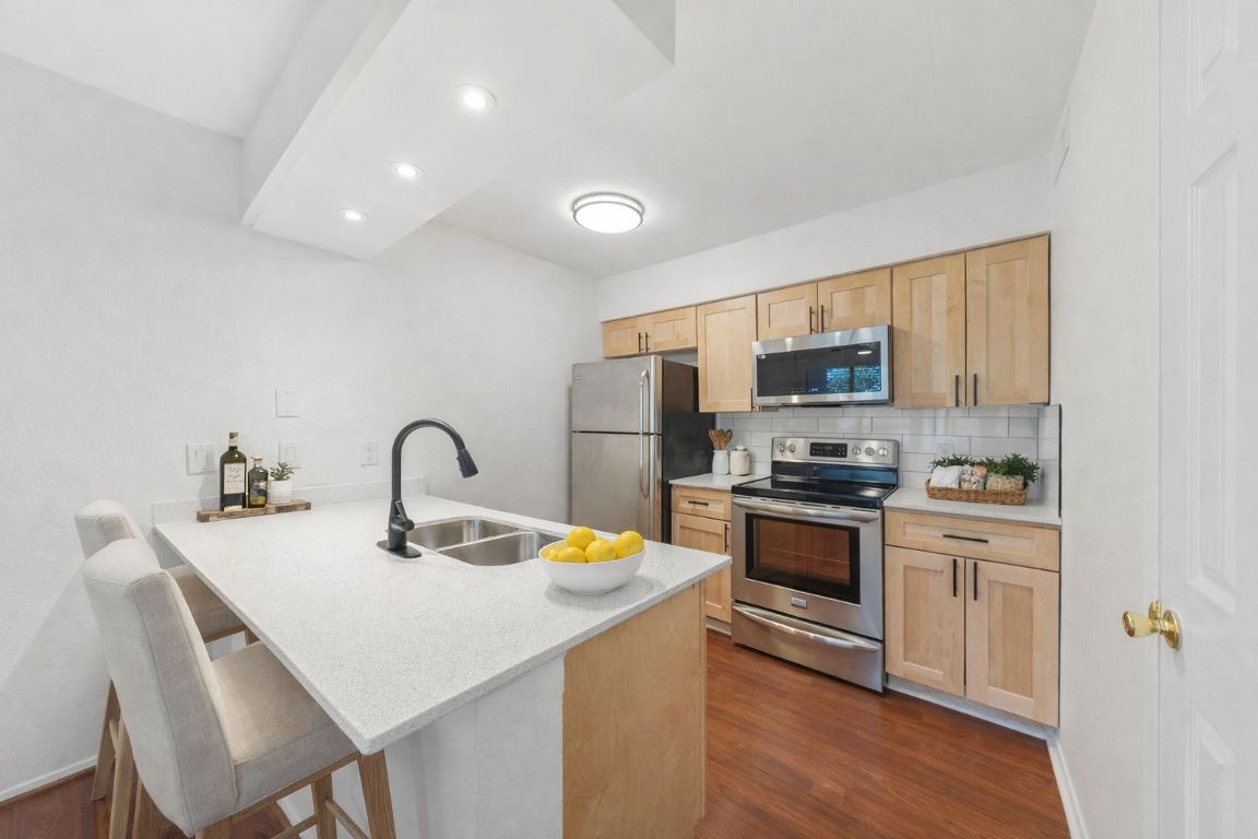 a kitchen with stainless steel appliances granite countertop a sink a stove a refrigerator with white cabinets and wooden floor