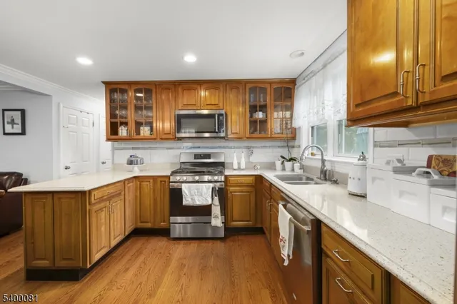 a kitchen with stainless steel appliances granite countertop wooden cabinets a sink a stove a refrigerator and microwave with wooden floor