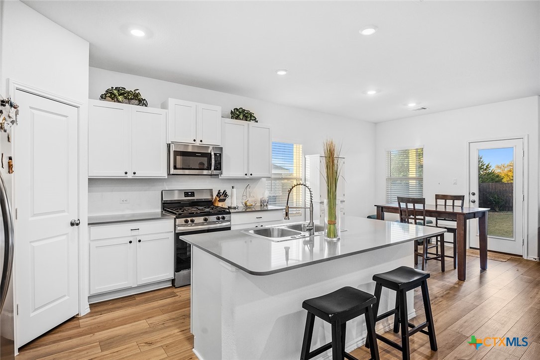 1909 Four Waters Loop Georgetown, TX 78628 - Photo 7 of 35 a kitchen with stainless steel appliances granite countertop a stove top oven a sink a refrigerator and white cabinets with wooden floor