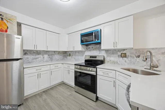 a kitchen with stainless steel appliances granite countertop white cabinets a sink a stove a refrigerator and white cabinets