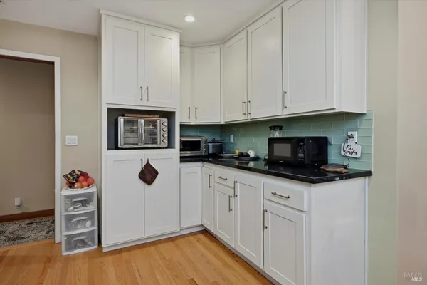 a kitchen with granite countertop a stove a sink and a white cabinets with wooden floor