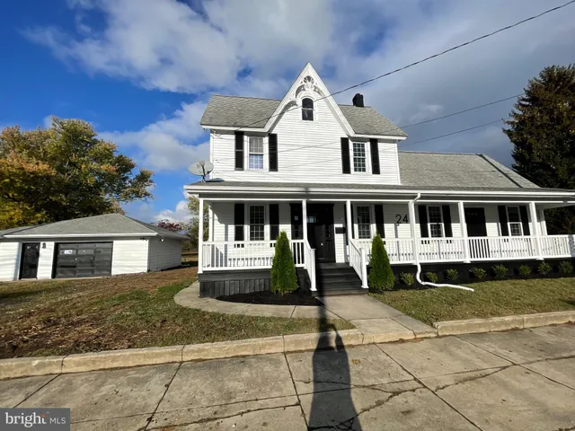 a white house that has a big yard with plants and large trees